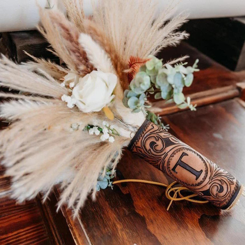 Bridal bouquet with pampas grass and a tooled leather handle wrap on wood.