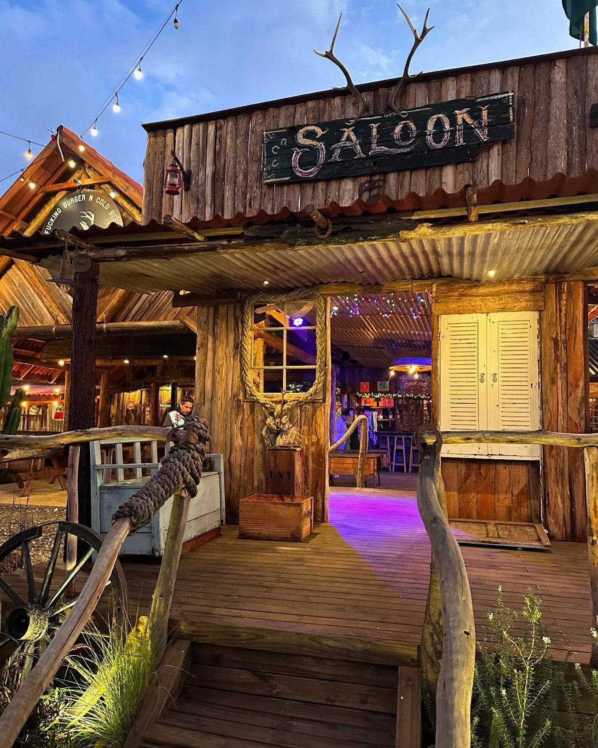 Rustic wooden saloon building with a sign and a lit interior bar area.