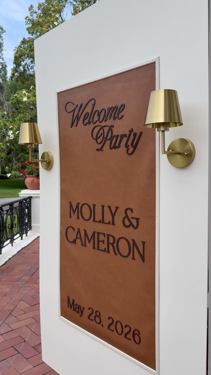Brown leather welcome sign for Molly and Cameron's party on a white wall.