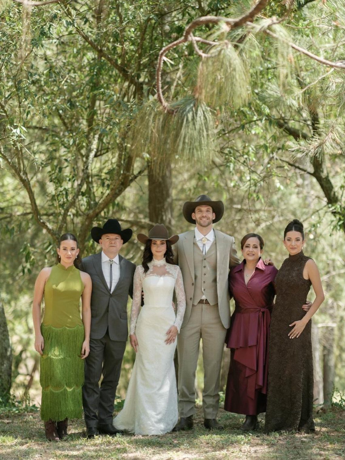 Wedding party posing in a wooded area with the couple wearing cowboy hats.