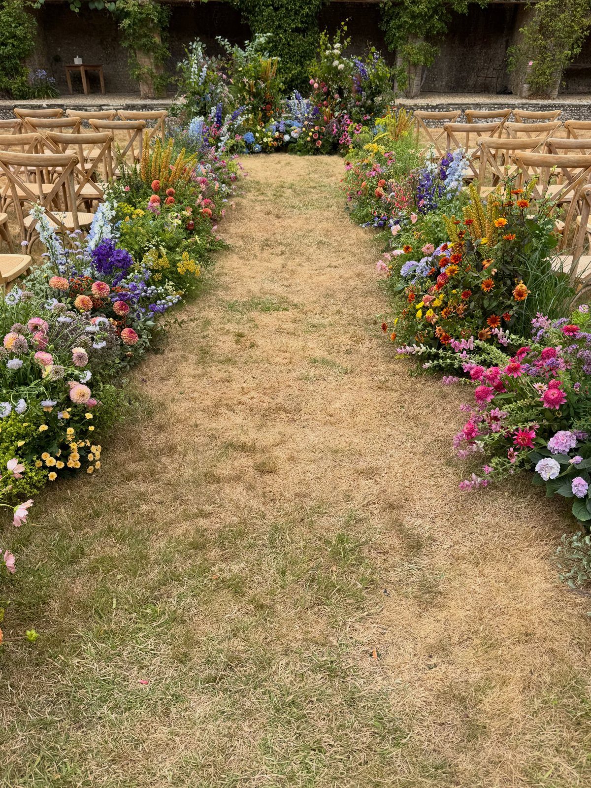 Whimsical Wildflower Wedding: 7 Decor Ideas That Feel Grown, Not Styled 7 A grassy wedding aisle lined with colorful wildflower arrangements and wooden chairs for guests.