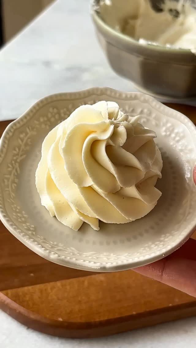9 White Buttercream Cake Ideas That Look Bakery-Worthy at Home 2 A swirl of white buttercream frosting on a small decorative ceramic plate held by a hand.
