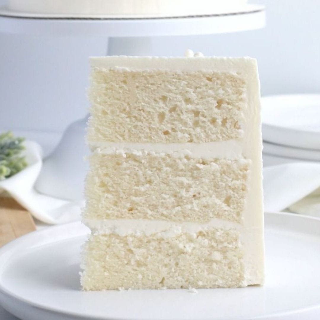 9 White Buttercream Cake Ideas That Look Bakery-Worthy at Home 5 A slice of three-layer white cake with creamy frosting on a white plate.