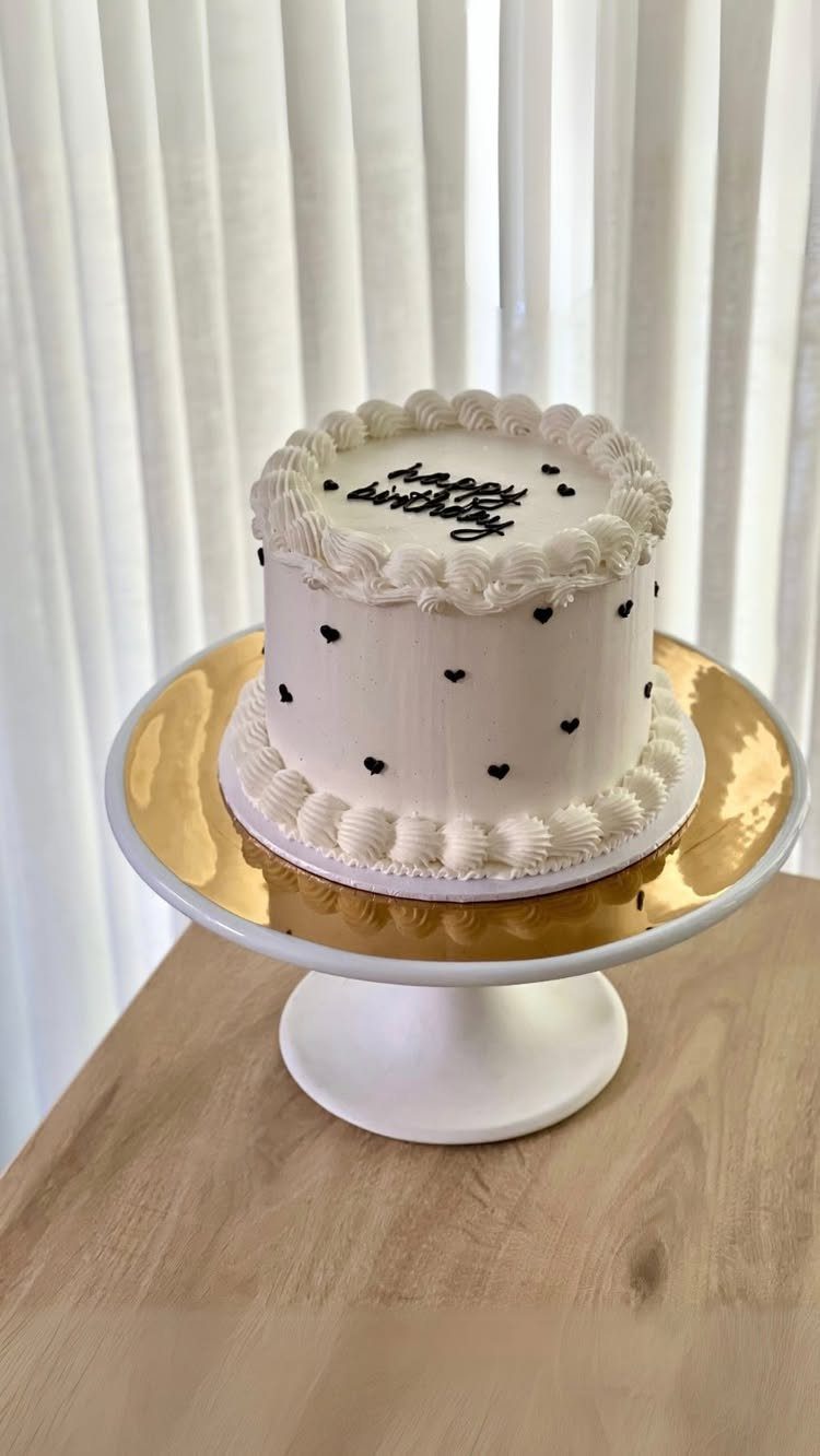 9 White Buttercream Cake Ideas That Look Bakery-Worthy at Home 10 White buttercream birthday cake with black heart decorations on a white cake stand.