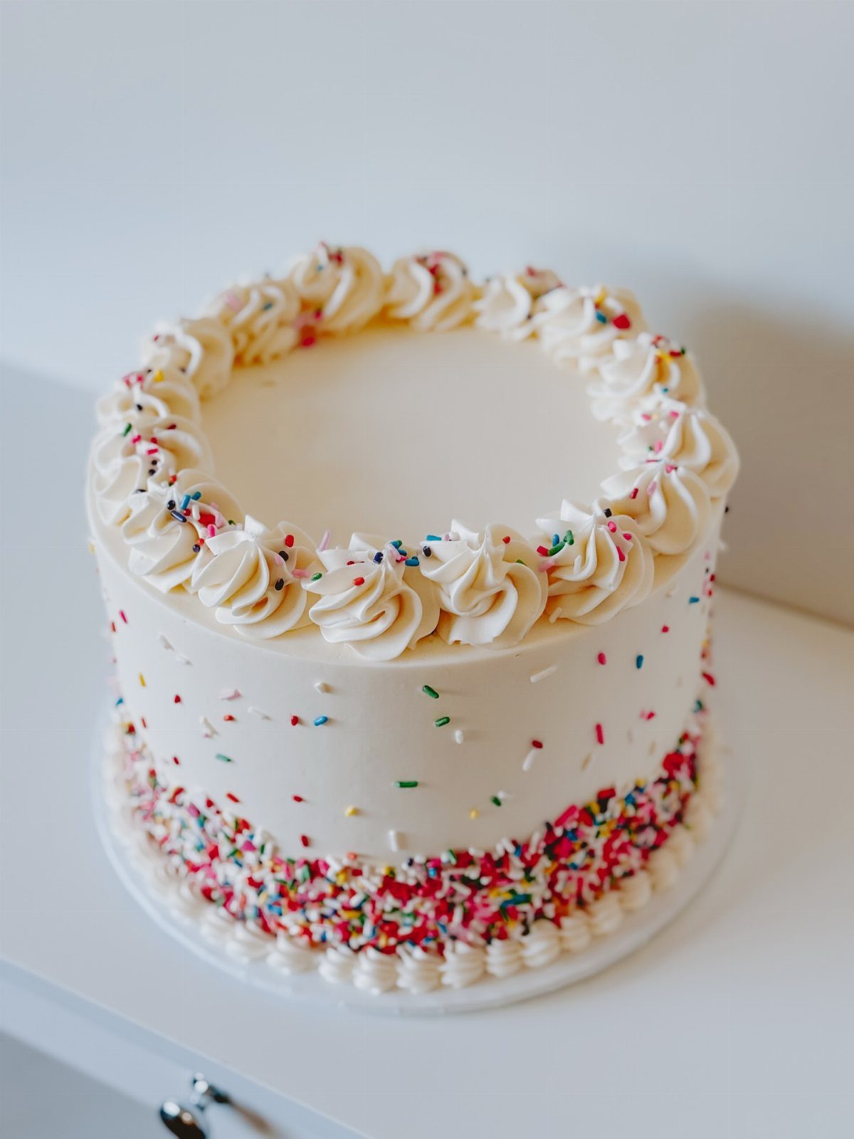 9 White Buttercream Cake Ideas That Look Bakery-Worthy at Home 3 A white buttercream cake decorated with colorful sprinkles around the base and sides.