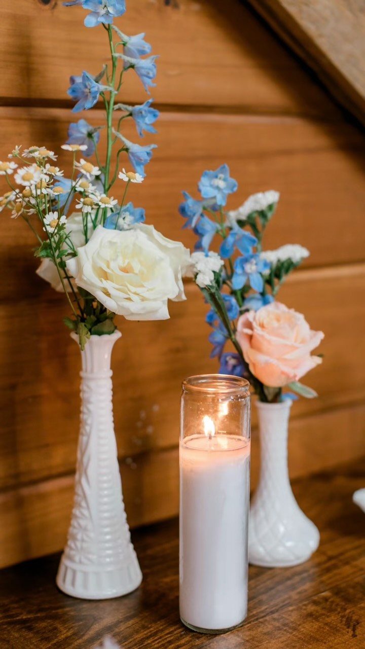 White Wedding Ideas: 23 Elegant Details for Your Big Day 21 White milk glass vases with blue and white flowers and a lit candle.