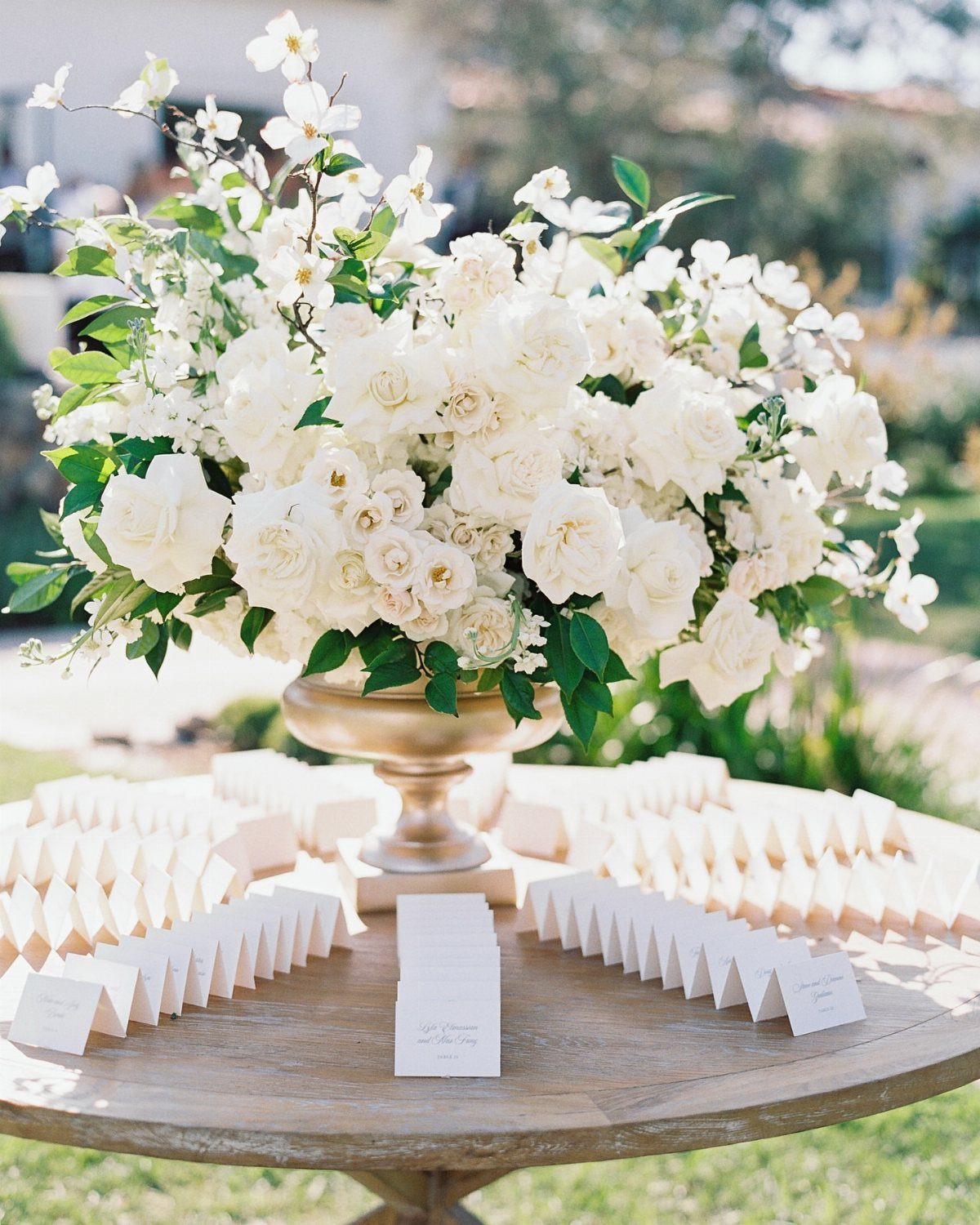 White Wedding Ideas: 23 Elegant Details for Your Big Day 20 White rose bouquet in gold vase on a table with white escort cards.