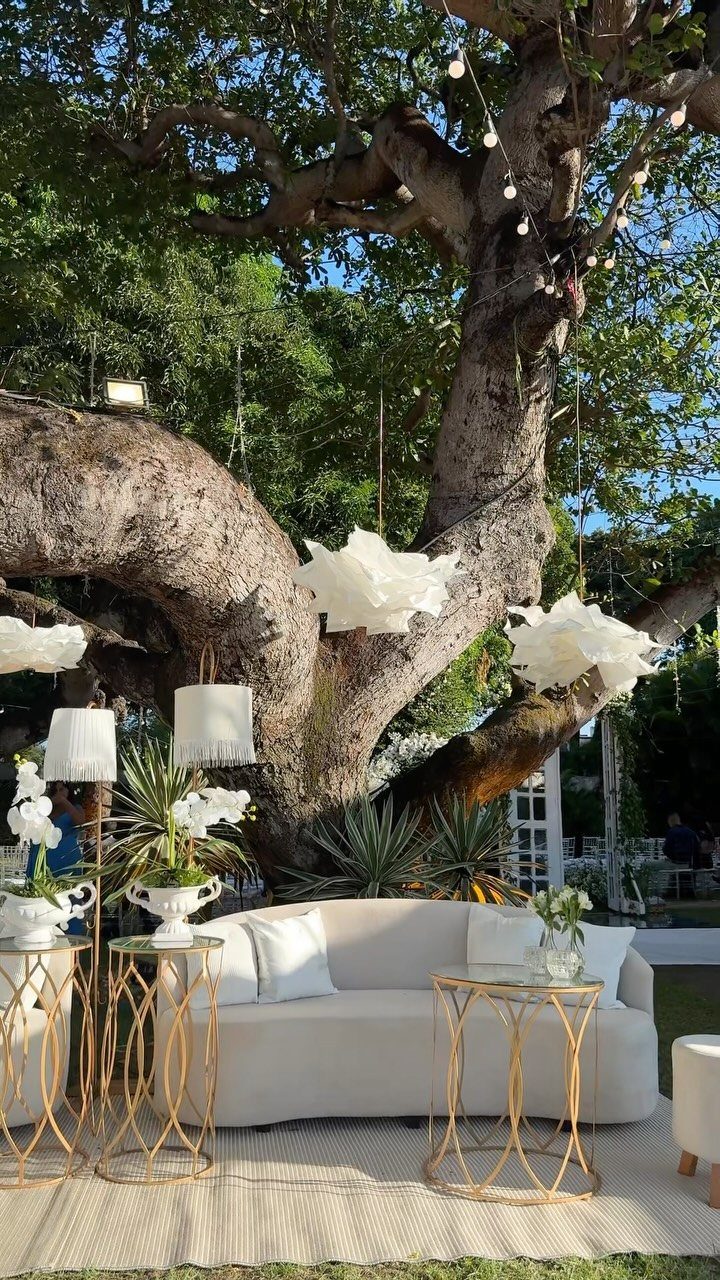 White Wedding Ideas: 23 Elegant Details for Your Big Day 7 White curved sofa and gold side tables in an outdoor lounge under a tree.