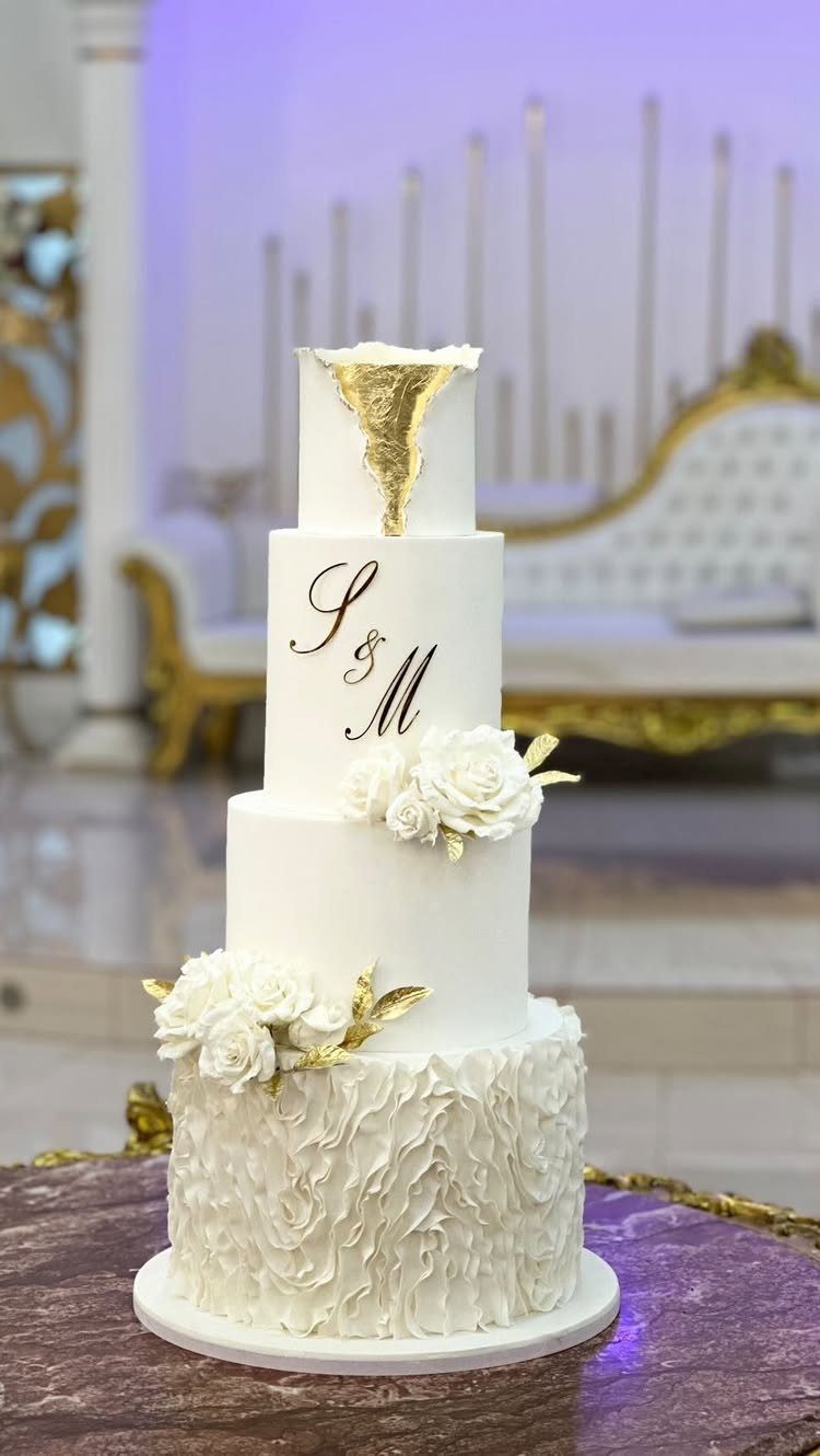 White Wedding Ideas: 23 Elegant Details for Your Big Day 2 Four-tier white wedding cake with gold accents, white roses, and gold initials.