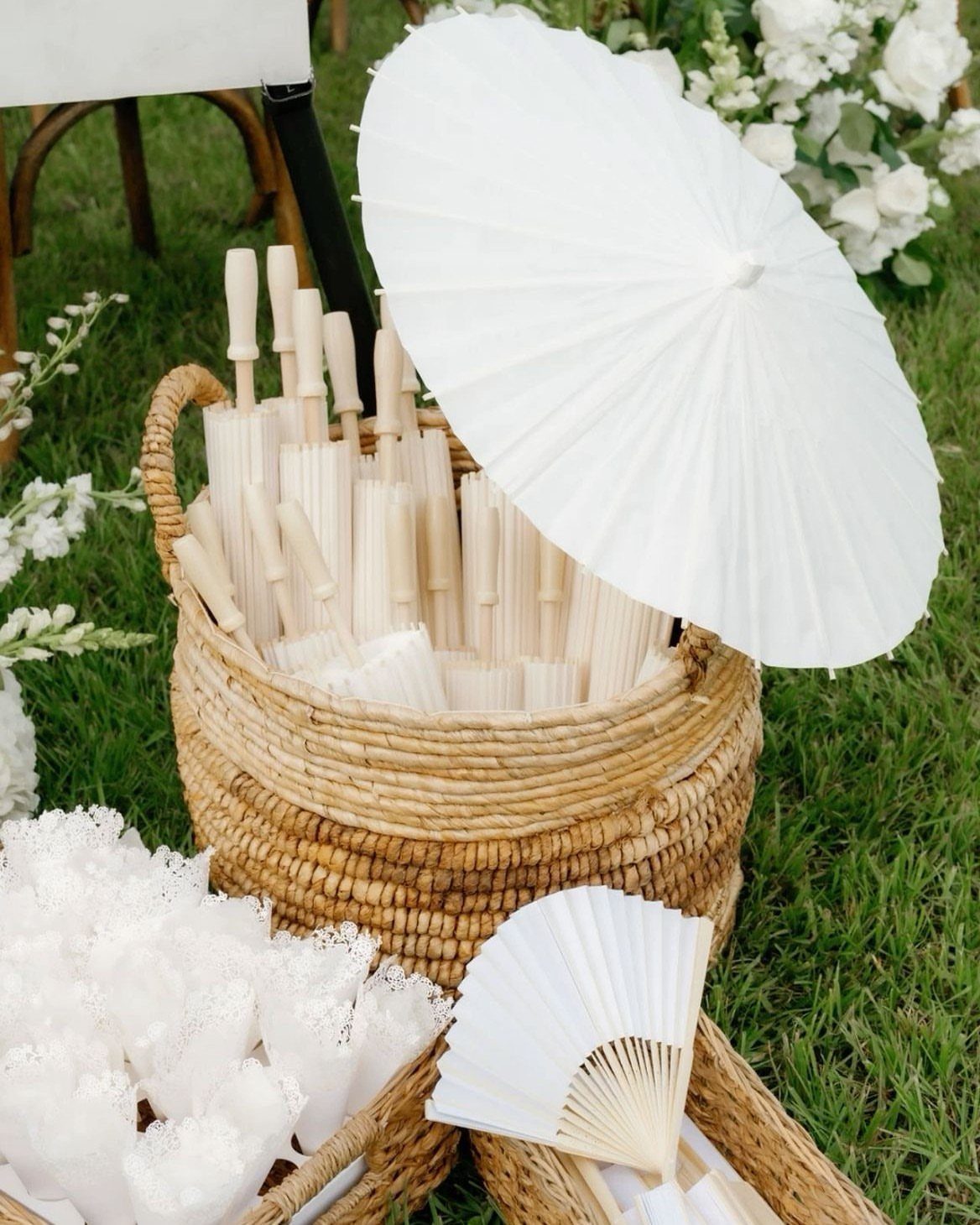 White Wedding Ideas: 23 Elegant Details for Your Big Day 23 White wedding parasols and folding fans arranged in woven wicker baskets on green grass.