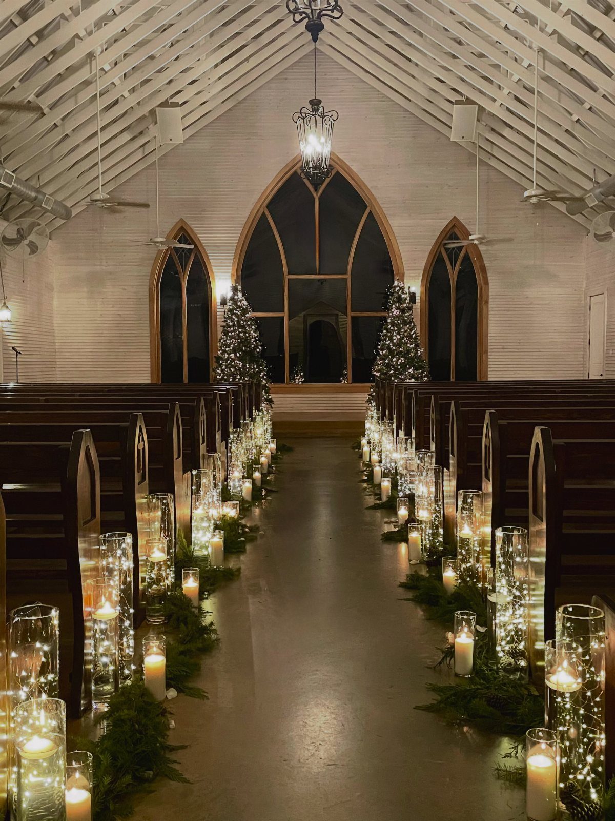 Church aisle decorated with candles, fairy lights, and evergreen greenery for a winter wedding.