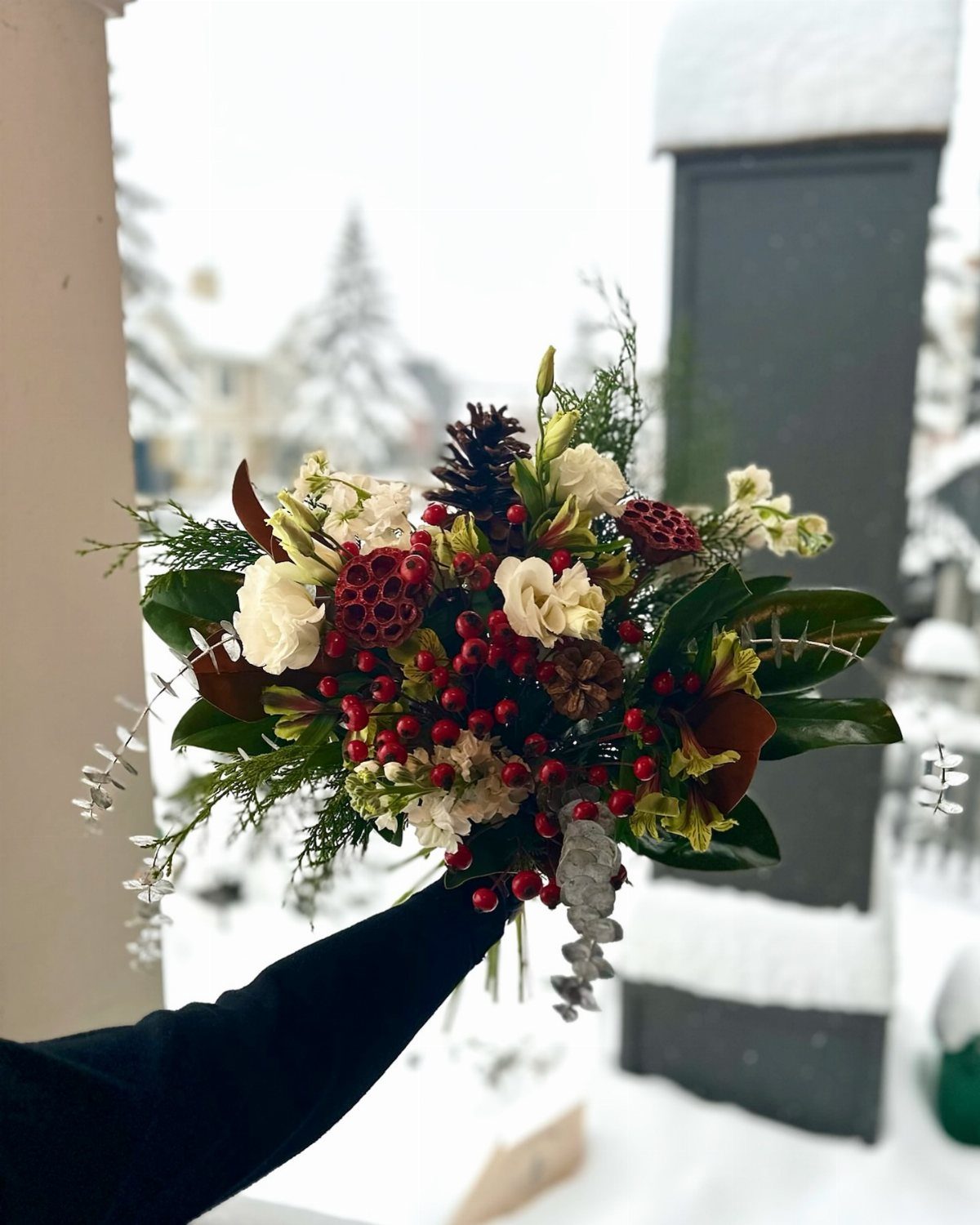 Winter bridal bouquet with white roses, red berries, and pinecones in snowy setting