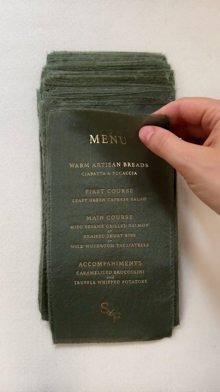 Dark green velvet menu with gold text held by a hand over a stack.