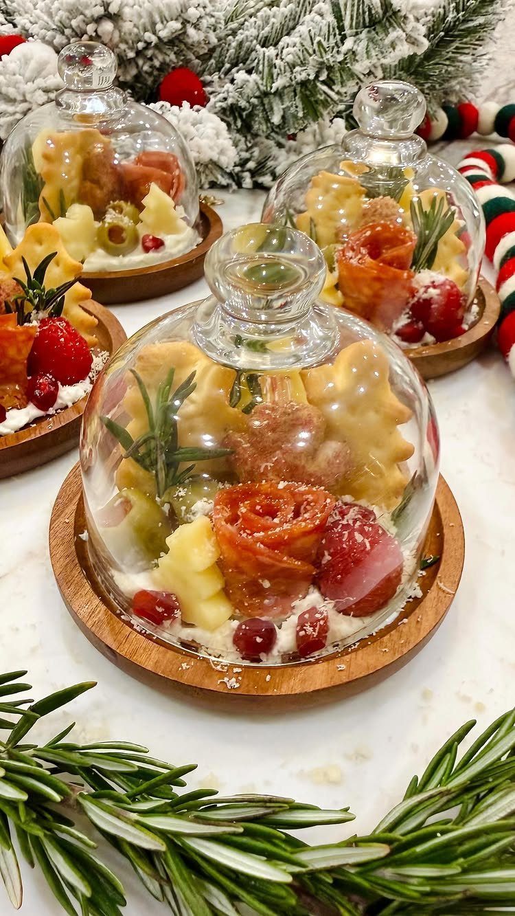 Charcuterie boards with meats and fruits under glass cloches with snowy winter greenery.